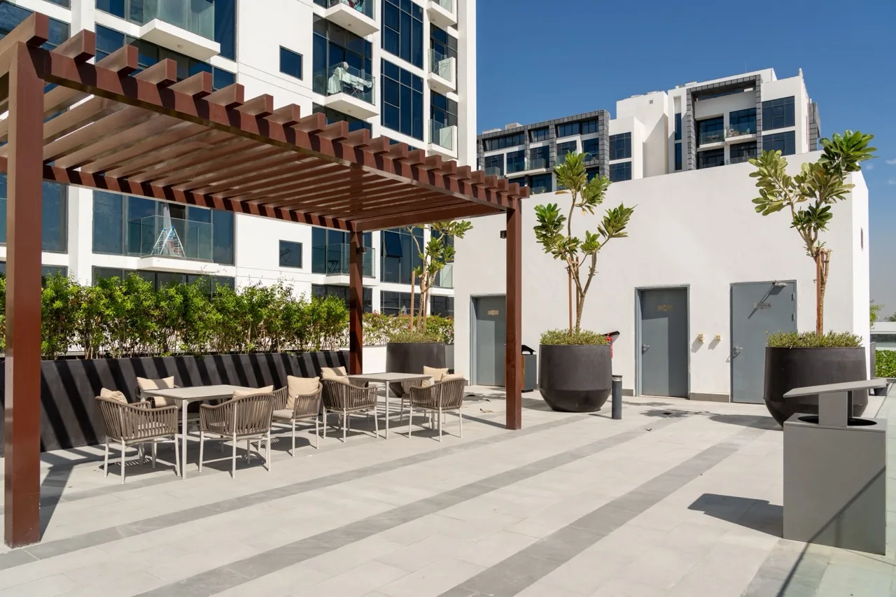 A hotel terrace with a pergola, lounge seating and planters, overlooked by the property's buildings